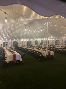 a lit tent with multiple long tables set with white tablecloths and centerpieces